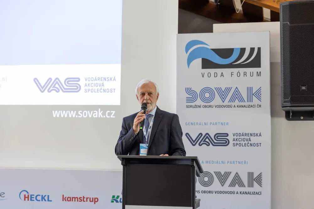 Muž hovoří u řečnického pultu, zahajuje konferenci
