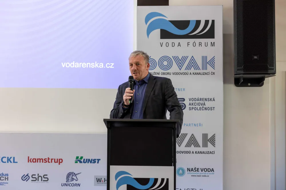 Muž hovoří u řečnického pultu, zahajuje konferenci